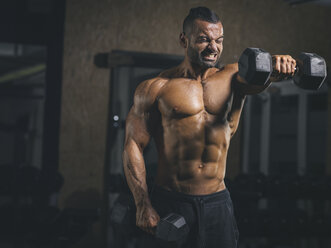 Bodybuilder beim Schultertraining im Fitnessstudio, bei dem er Kurzhanteln nach vorne hebt - MADF000772