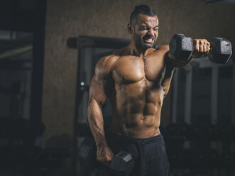 Bodybuilder performing dumbbell front raises in his shoulder workout in gym - MADF000772