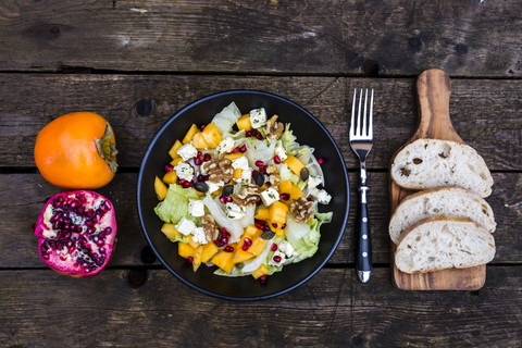 Autumnal salad with kaki, feta cheese, iceberg lettuce, pumpkin seeds, pomegranate and walnuts stock photo