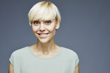 Portrait of smiling blond woman in front of grey background - RH001057