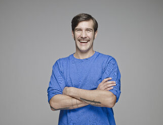 Porträt eines lachenden Mannes mit verschränkten Armen vor einem grauen Hintergrund - RH001069