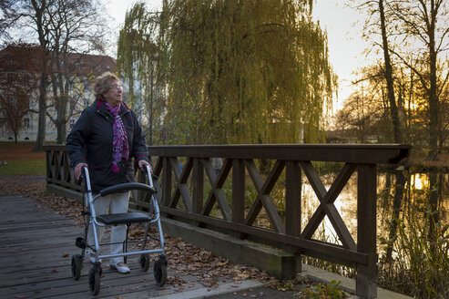 Senior woman with wheeled walker walking on footbridge in the evening - FRF000368