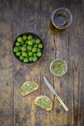 Schale mit grünen Oliven, Karaffe mit Olivenöl, Messer und Brotscheiben mit Olivenaufstrich - LVF004279