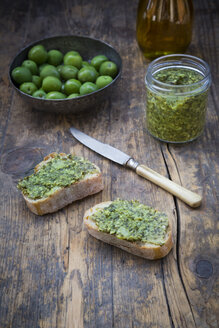 Schale mit grünen Oliven, Karaffe mit Olivenöl, Messer und Brotscheiben mit Olivenaufstrich - LVF004280