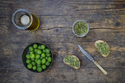Schale mit grünen Oliven, Karaffe mit Olivenöl, Messer und Brotscheiben mit Olivenaufstrich - LVF004281