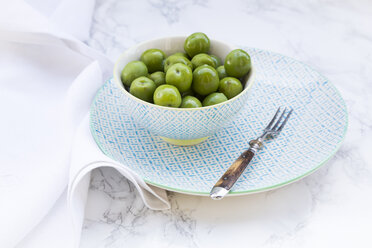 Bowl of green olives and fork on plate and white marble - LVF004291