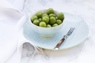 Schale mit grünen Oliven und Gabel auf Teller und weißem Marmor - LVF004291