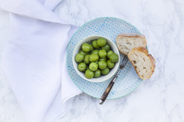 Bowl of green olives, fork and slices of bread on plate - LVF004292