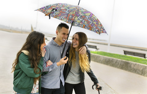 Drei glückliche Freunde gehen mit Regenschirm die Straße entlang, lizenzfreies Stockfoto