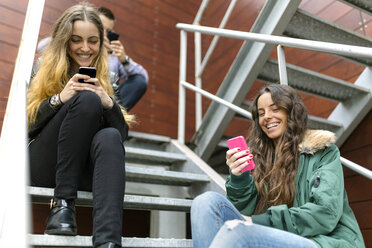 Drei Freunde hängen mit ihren Handys im Freien herum - MGOF001143