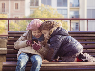 Mädchen und Junge in Winterkleidung spielen mit Smartphone - XCF000043