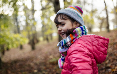 Glückliches kleines Mädchen im Wald mit Mütze und Schal im Herbst - MGOF001159