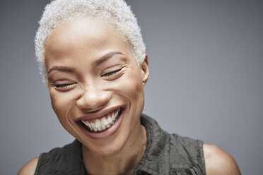 Porträt einer lachenden Frau mit geschlossenen Augen vor einem grauen Hintergrund - RHF001083