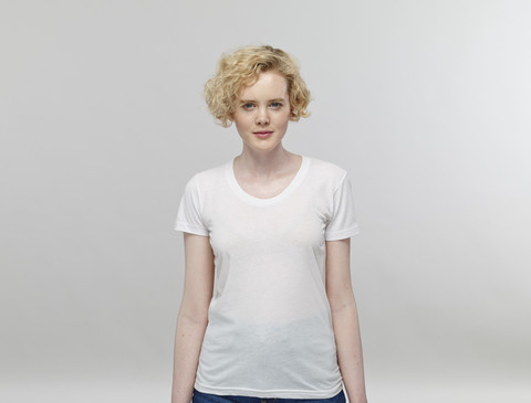 Portrait of blond woman wearing white t-shirt in front of grey background stock photo