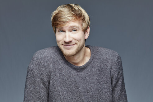 Portrait of smiling blond man in front of grey background - RHF001097