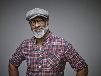 Portrait of smiling man wearing cap and spectacles in front of grey background - RHF001103