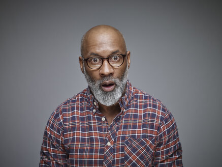 Portrait of astonished man wearing spectacles and checked shirt in front of grey background - RHF001105