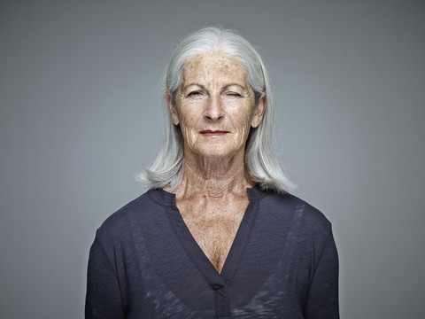 Portrait of senior woman with grey hair in front of grey background stock photo