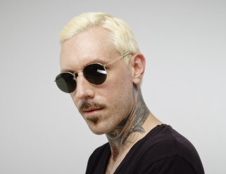 Porträt eines Mannes mit Tätowierung und blond gefärbtem Haar, der eine Sonnenbrille trägt - RHF001124