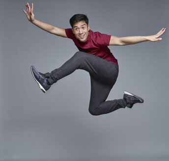 Porträt eines jungen Mannes, der vor einem grauen Hintergrund in die Luft springt - RHF001129