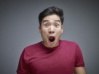 Porträt eines schockierten jungen Mannes vor einem grauen Hintergrund - RHF001130