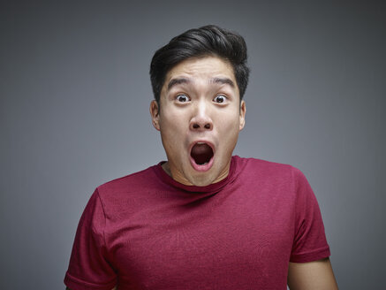 Portrait of shocked young man in front of grey background - RHF001130