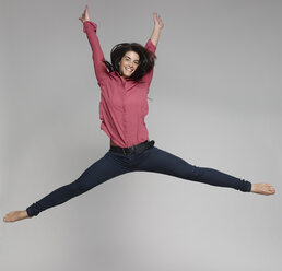 Porträt einer jungen Frau, die vor einem grauen Hintergrund in die Luft springt - RHF001141
