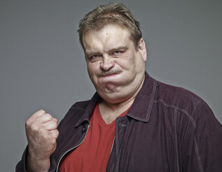 Portrait of man clenching his fist in front of grey background - RHF001143