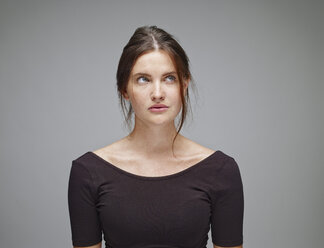 Porträt einer jungen Frau, die vor einem grauen Hintergrund aufblickt - RHF001144
