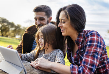 Glückliche Eltern mit Tochter, die im Freien ein digitales Tablet benutzt - MGOF001179