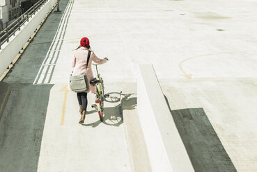 Junge Frau schiebt ihr Fahrrad auf einem Parkdeck - UUF006175