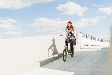 Junge Frau fährt Fahrrad und hält ein Handy in der Hand - UUF006176