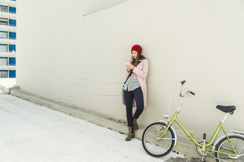 Junge Frau neben dem Fahrrad schaut auf ihr Handy, lizenzfreies Stockfoto