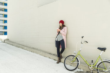 Junge Frau neben dem Fahrrad schaut auf ihr Handy - UUF006187