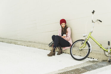 Junge Frau sitzt neben dem Fahrrad und schaut auf ihr Handy - UUF006188