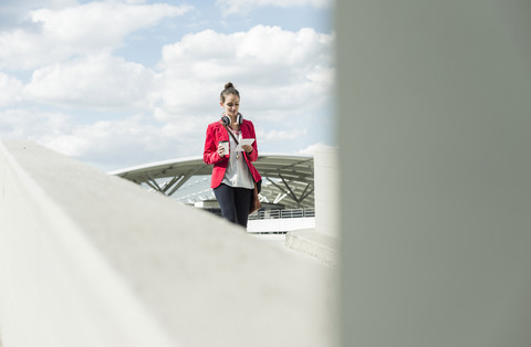 Junge Frau mit Coffee to go, Kopfhörern und Phablet auf dem Parkdeck, lizenzfreies Stockfoto