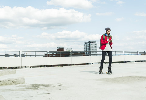 Junge Frau mit Mobiltelefon und Inline-Skates auf dem Parkdeck, lizenzfreies Stockfoto