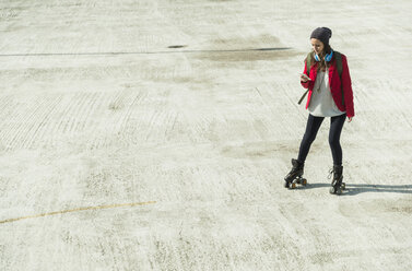 Young woman with cell phone and inline skates on parking level - UUF006207