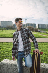 Smiling young man with longboard wearing mirrored sunglasses - RAEF000720