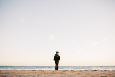 Rückenansicht einer jungen Frau, die im Winter am Strand steht - JRFF000237