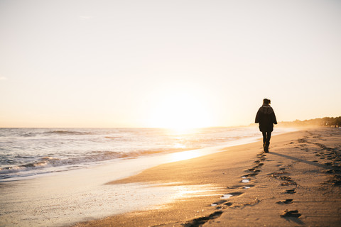 Back view of young woman walking on the beach in winter stock photo