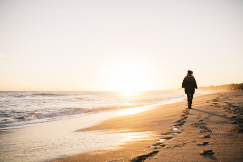 Rückenansicht einer jungen Frau, die im Winter am Strand spazieren geht, lizenzfreies Stockfoto