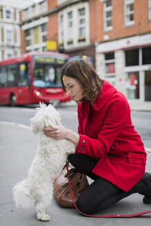 UK, London, junge Frau kniet auf dem Bürgersteig mit dem Gesicht zu ihrem Hund - MAUF000145