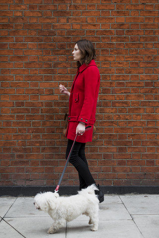 Junge Frau in roter Jacke geht mit ihrem Hund spazieren, lizenzfreies Stockfoto