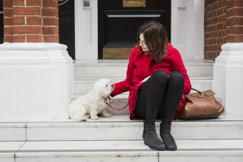 UK, London, junge Frau sitzt auf einer Treppe neben ihrem Hund, lizenzfreies Stockfoto