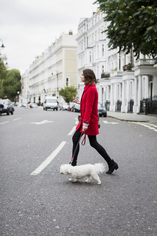 UK, London, junge Frau in roter Jacke überquert mit ihrem Hund die Straße, lizenzfreies Stockfoto