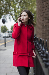 Großbritannien, London, Porträt einer jungen Frau in roter Jacke, die mit einem Smartphone telefoniert - MAUF000154