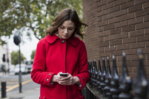Junge Frau in roter Jacke schaut auf ihr Smartphone - MAUF000155