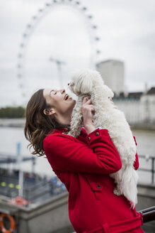 UK, London, glückliche junge Frau mit Hund auf dem Arm und London Eye im Hintergrund - MAUF000157