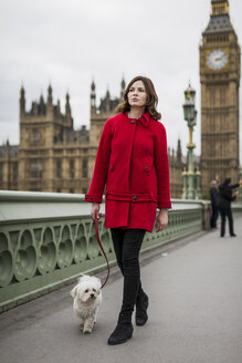 Junge Frau in roter Jacke geht mit ihrem Hund spazieren - MAUF000159